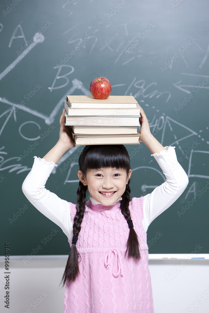 Happy little girl with textbooks and apple in classroom