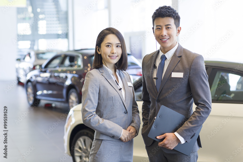 Confident salespeople standing with new cars in showroom