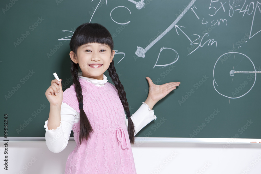 Cute little girl writing on blackboard