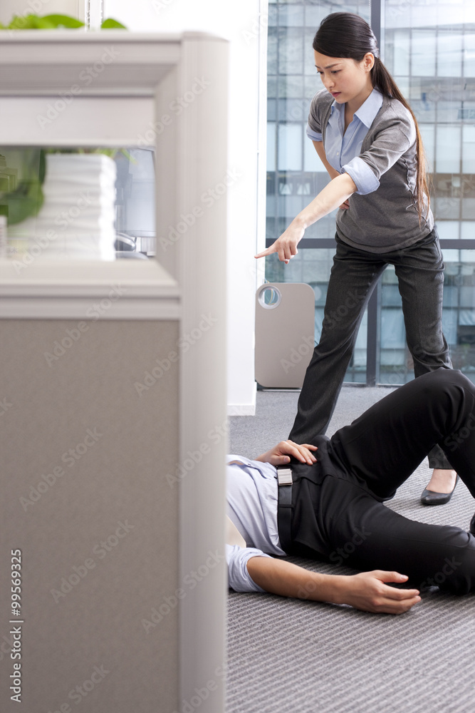 Businesswoman angrily pointing and accusing her colleague lying on the floor