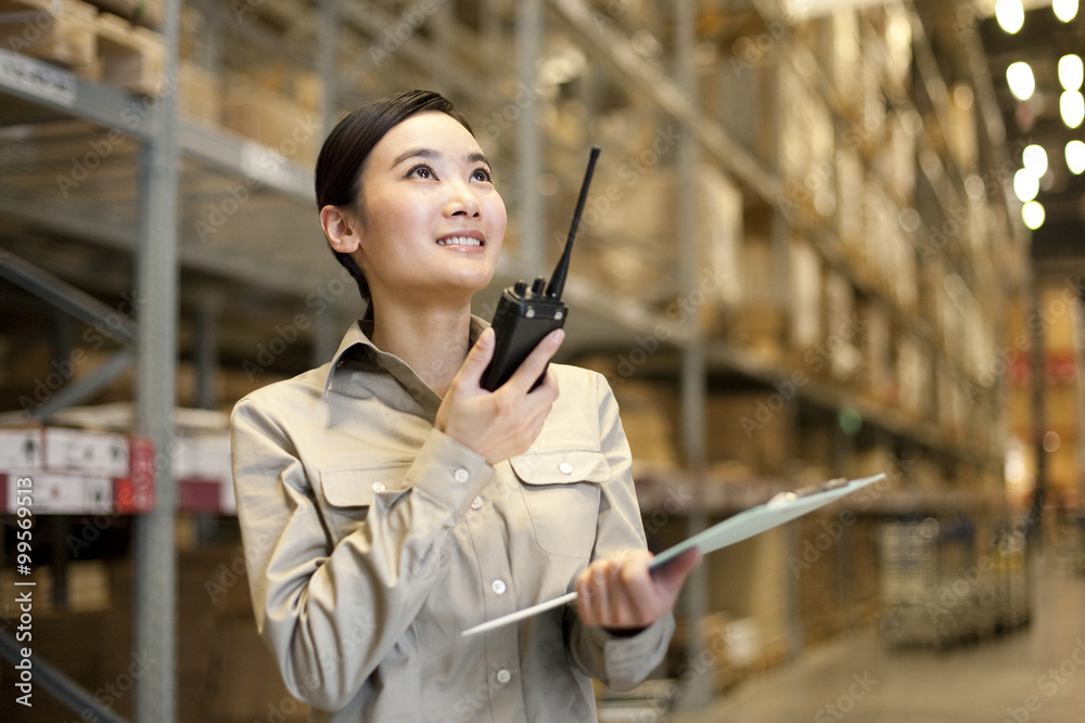 Female Chinese warehouse worker with clipboard and walkie-talke