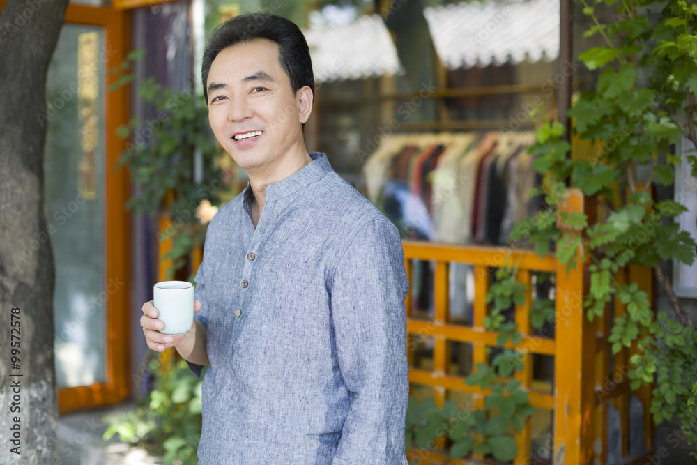 Male shopkeeper standing in doorway with a cup of tea