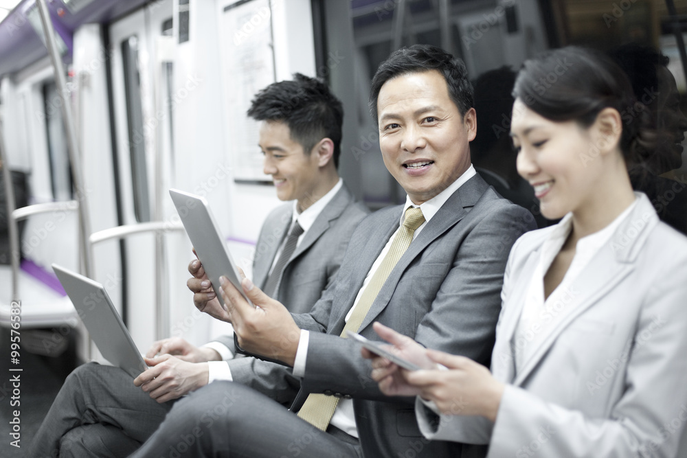 Business persons using digital products in subway train