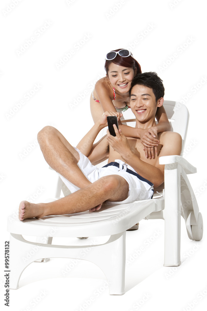 Young man and young woman in swimsuit using mobile phone