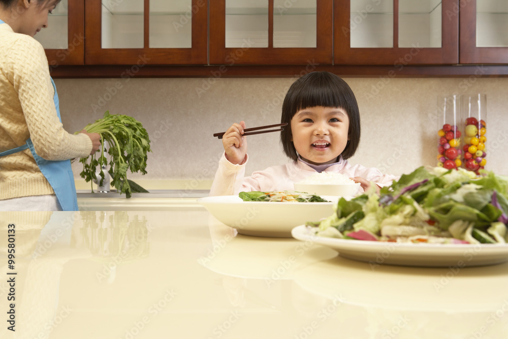 年轻女孩一边吃蔬菜，一边妈妈做饭