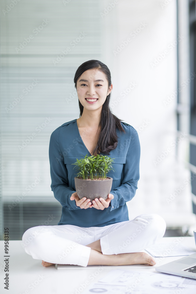 拿着盆栽坐在办公桌上的年轻女商人