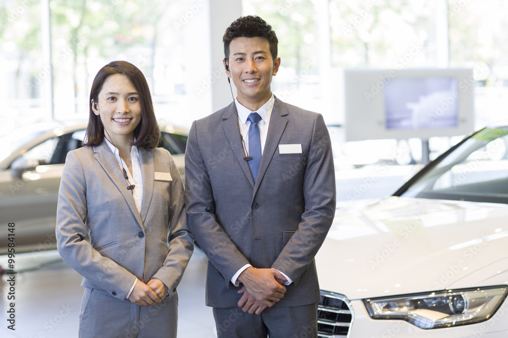 Confident salespeople standing with new cars in showroom