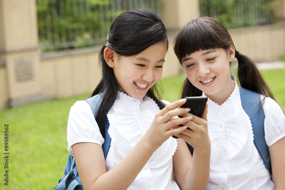 校园里穿着制服拿着智能手机的兴奋女学生