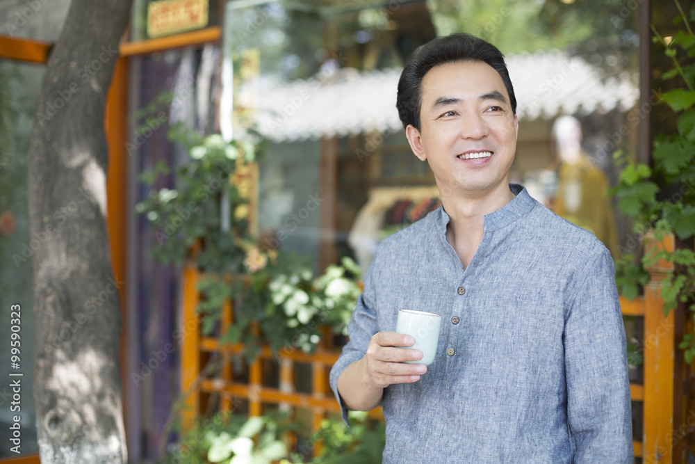 男店主端着一杯茶站在门口