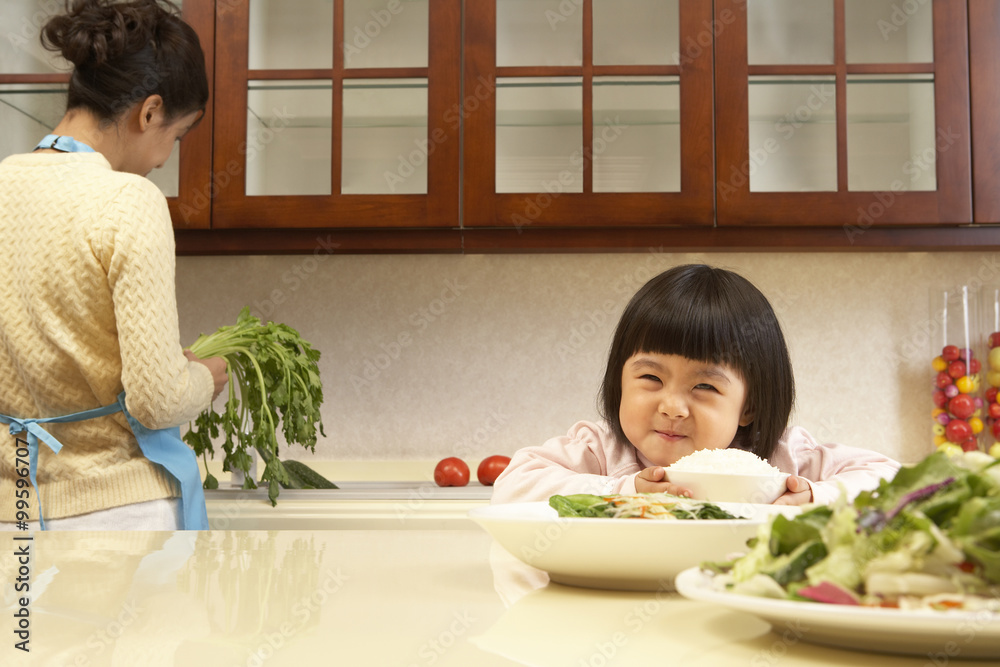 年轻女孩一边吃蔬菜，一边妈妈做饭