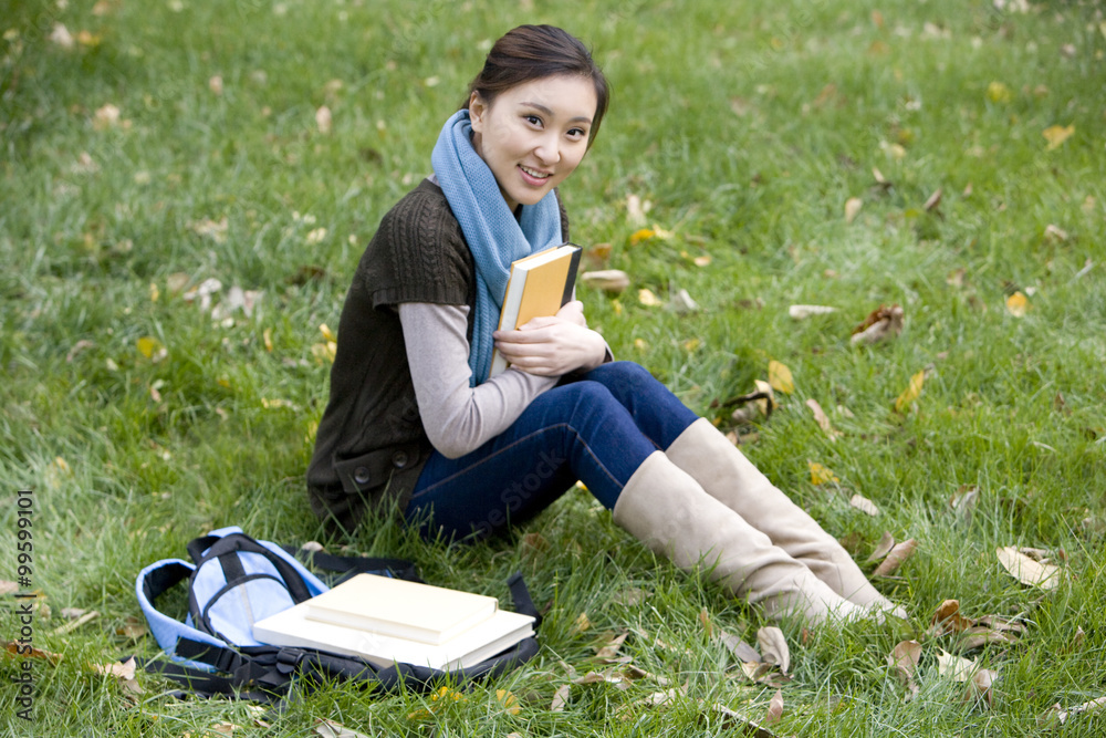 A young woman holding a book while sitting on a grassy area