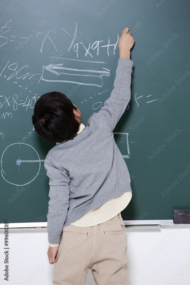 Happy little boy writing on blackboard