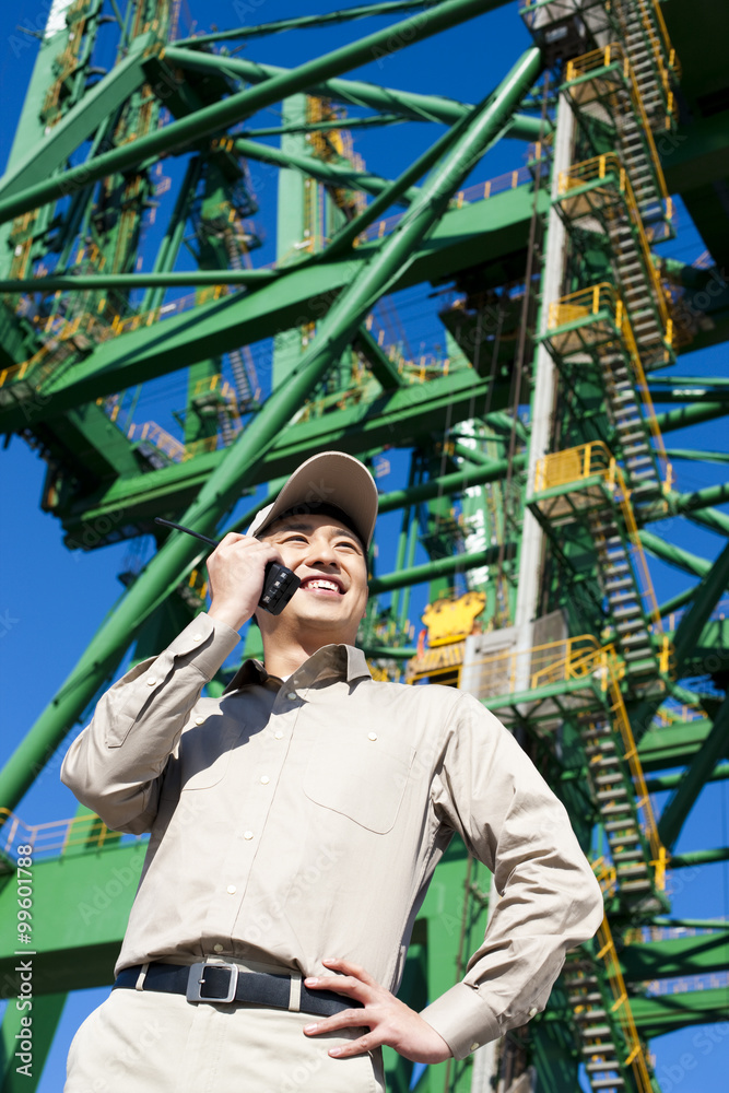 Male shipping industry worker with walkie talkie and crane in the background