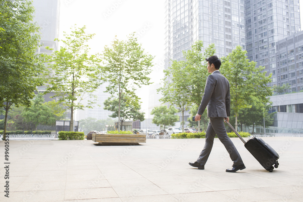 Young businessman pulling suitcase walking