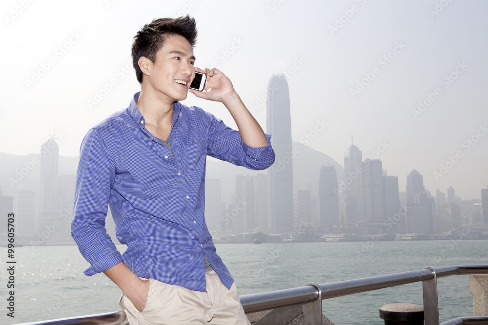 Happy young man talking on the phone in Victoria Harbor, Hong Kong