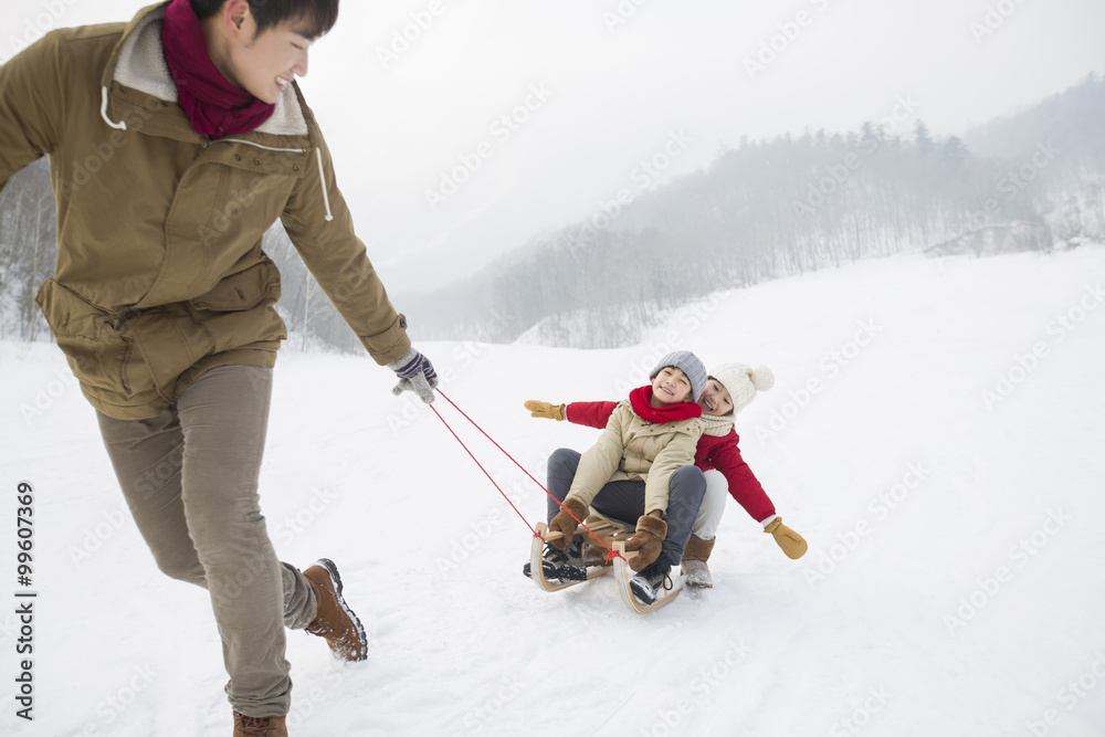 Young father pulling his children on sled