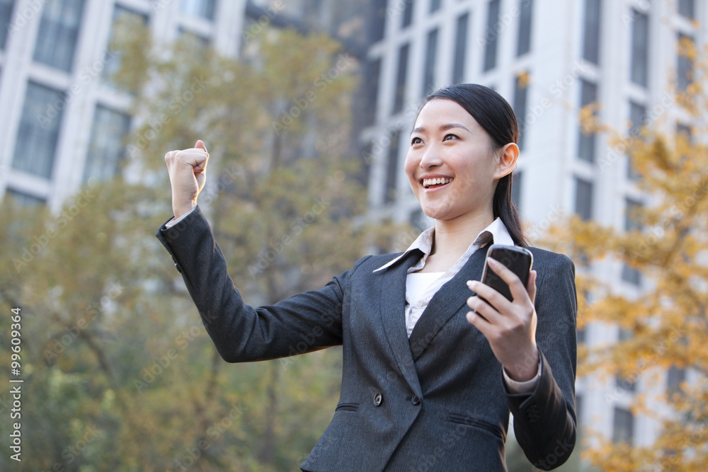 Businesswoman looking at her mobile phone and celebrating