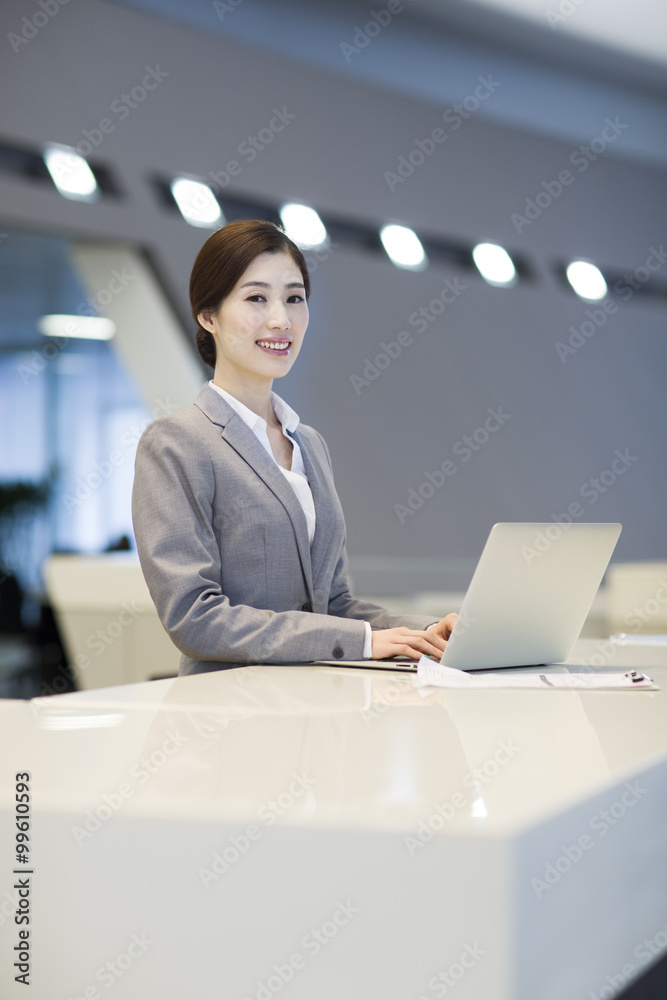 Confident receptionist using laptop at reception counter