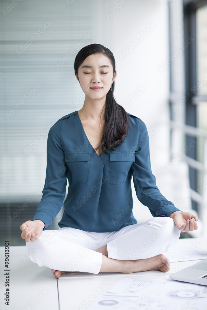 年轻女商人在办公桌上做瑜伽