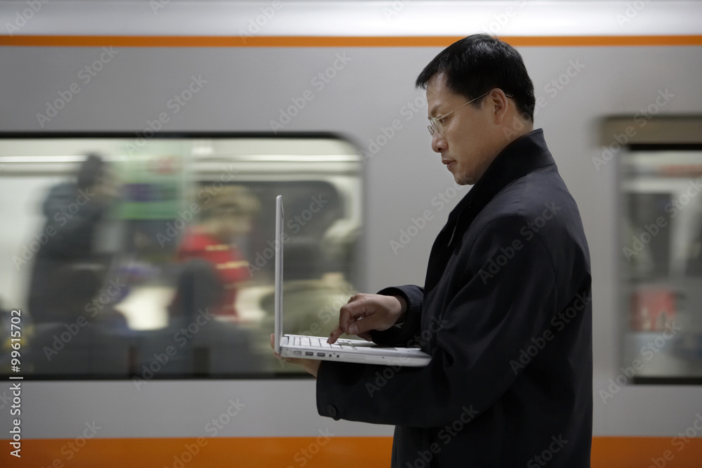 A Man Uses His Laptop As The Subway Train Passes By In The Background