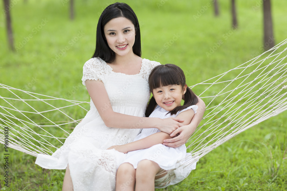 Happy young mother and daughter sitting in a hammock outdoors