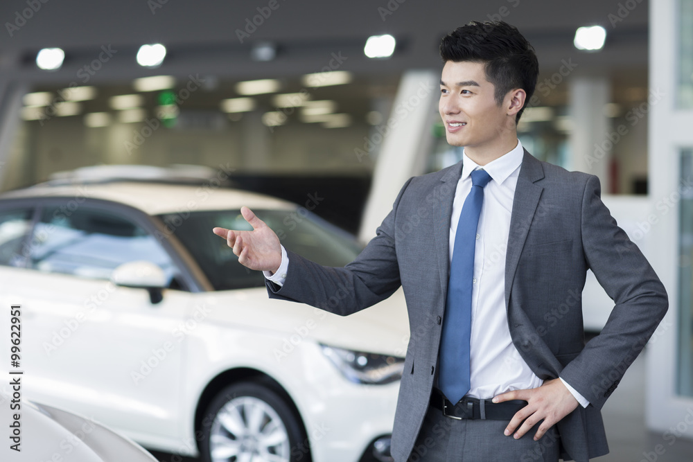 Confident salesman standing with new cars in showroom