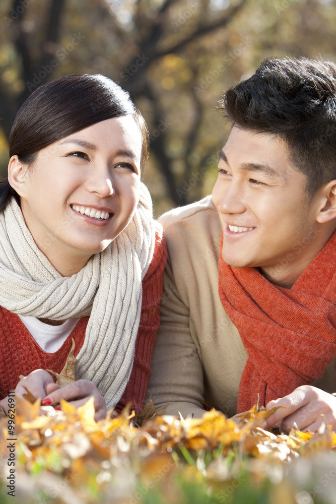 Young couple lying on the grass surrounded by Autumn leaves