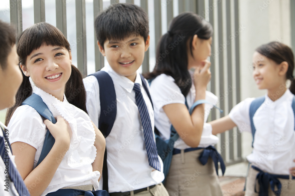 Cute schoolchildren in uniform leaning against a fence