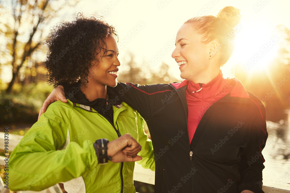 Two smiling sportswomen hugging while standing outdoors