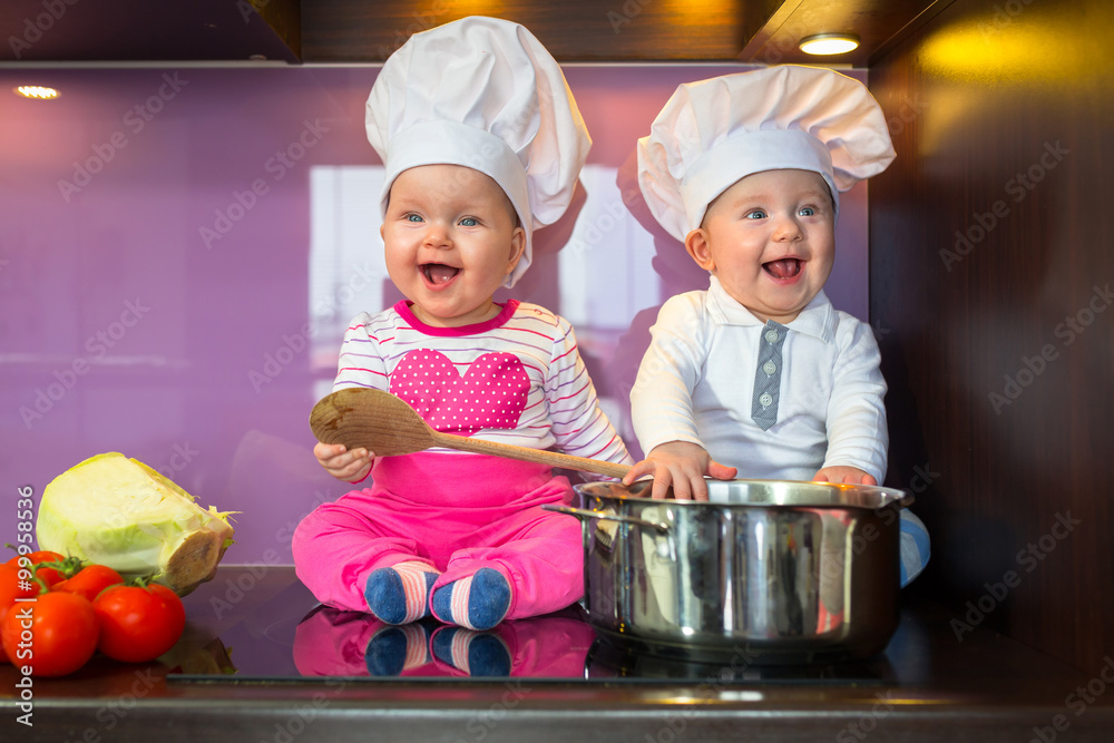 Little cook twins. Boy and girl in chef hat cooking at the kitchen.