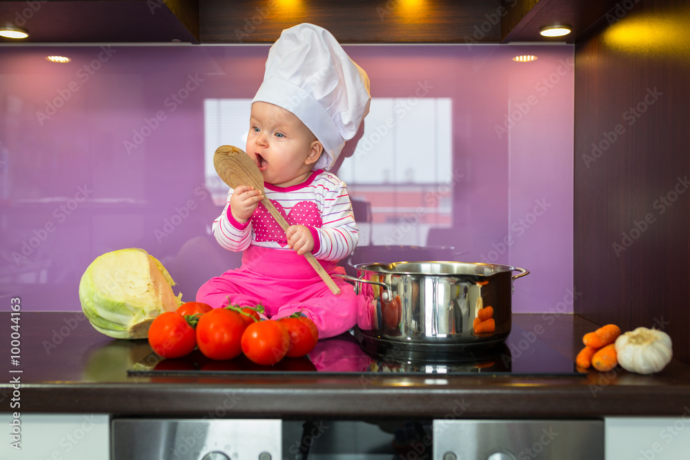 Little baby girl cook in chef hat at the kitchen