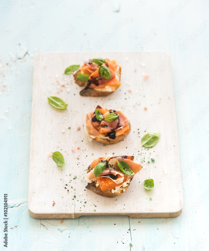 Bruschettas with Prosciutto, roasted melon, soft cheese and basil on wooden serving board over light