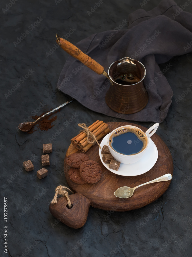 Cup of black coffee with chocolate biscuits, cinnamon sticks and cane sugar cubes on rustic wooden b