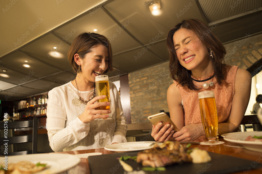 两个女人在餐厅喝啤酒前看着智能手机