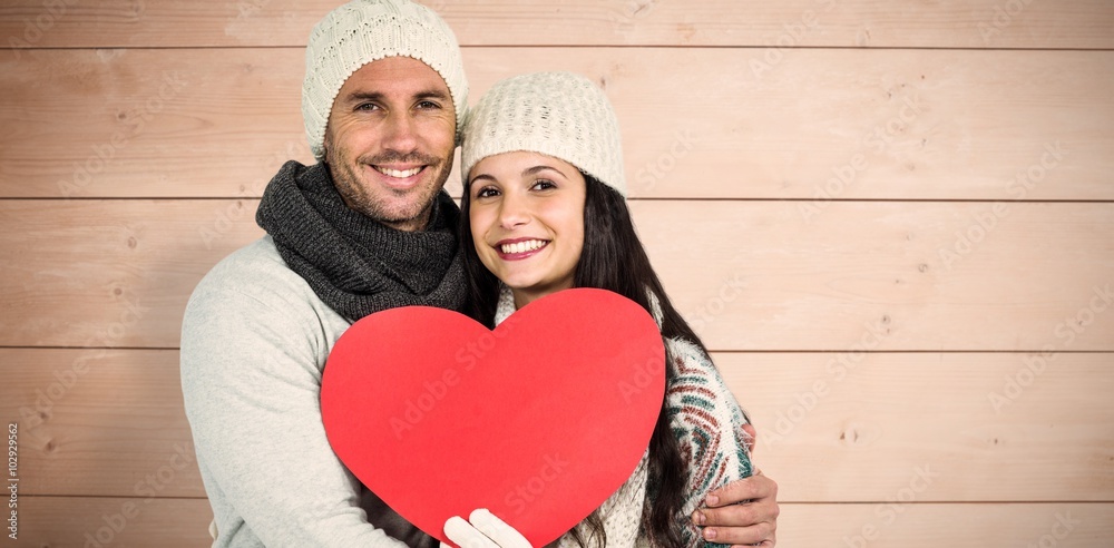 Composite image of smiling couple holding paper heart