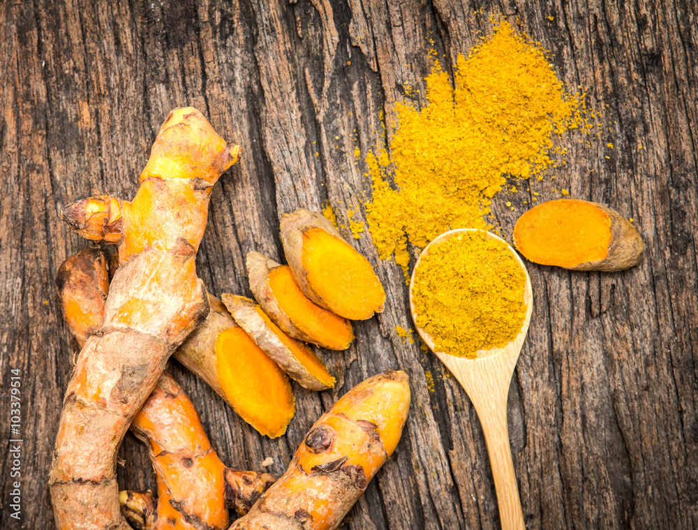 turmeric powder in spoon and roots on wooden plate