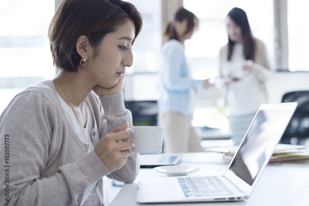 女人正拿着一杯咖啡看着笔记本电脑