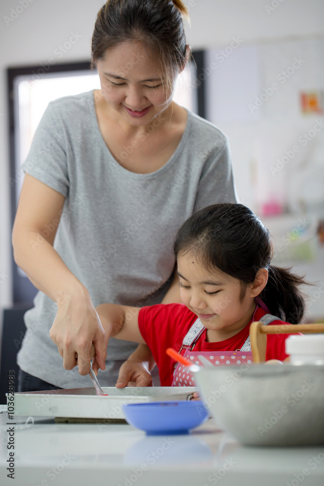 Little Asian cute chef cooking a bakery in kitchen with mother