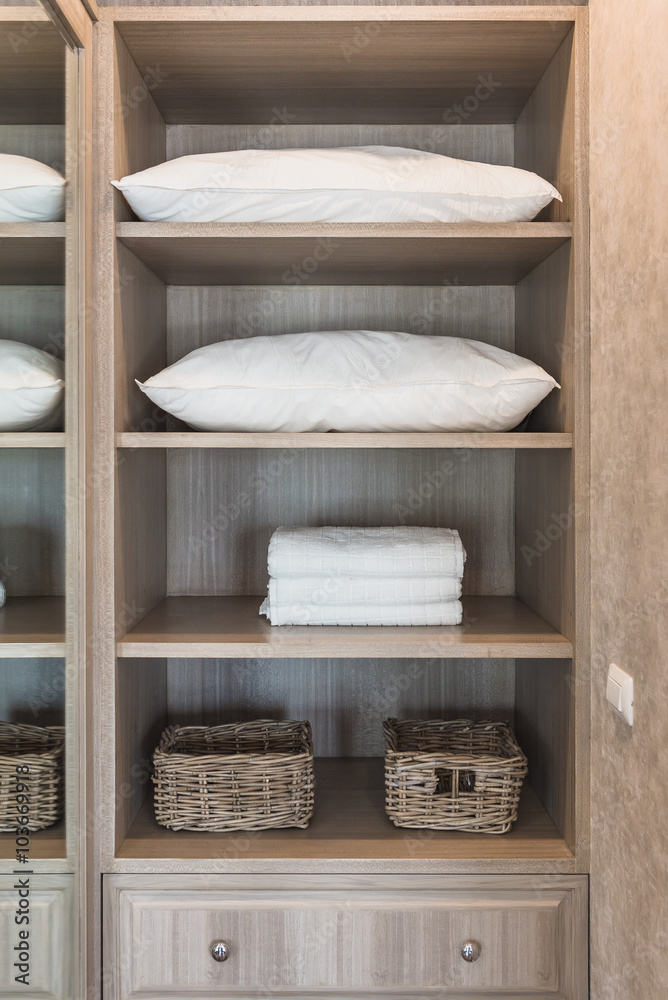 white towel and white pillow in wooden wardrobe with basket