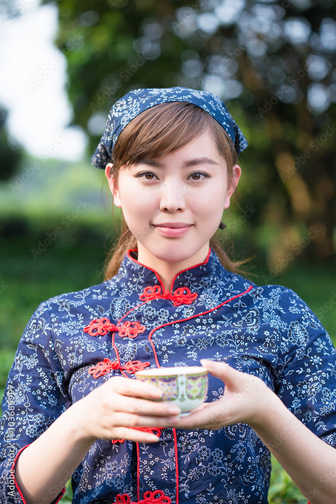 beautiful Asian girl holds cup in green tea plantation