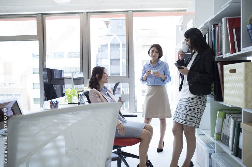 Three women are the stand talking in break time in the office