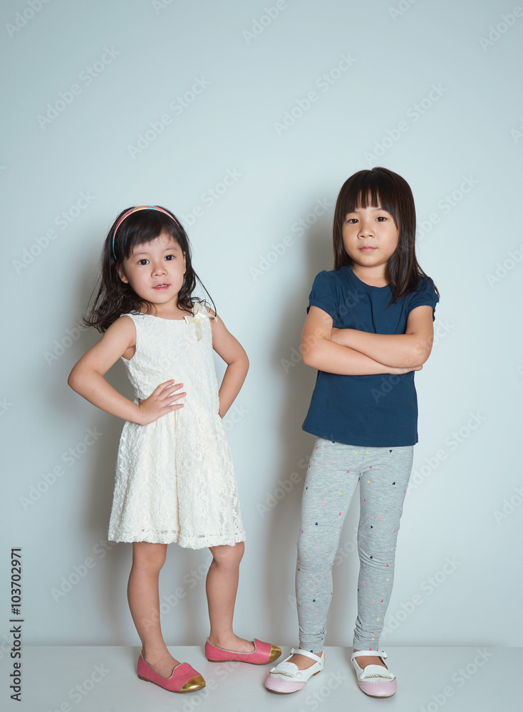 Two little asian sisters in a fashion pose on plain background