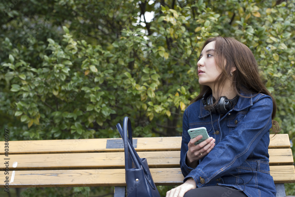 年轻女性在公园里等朋友坐在长椅上