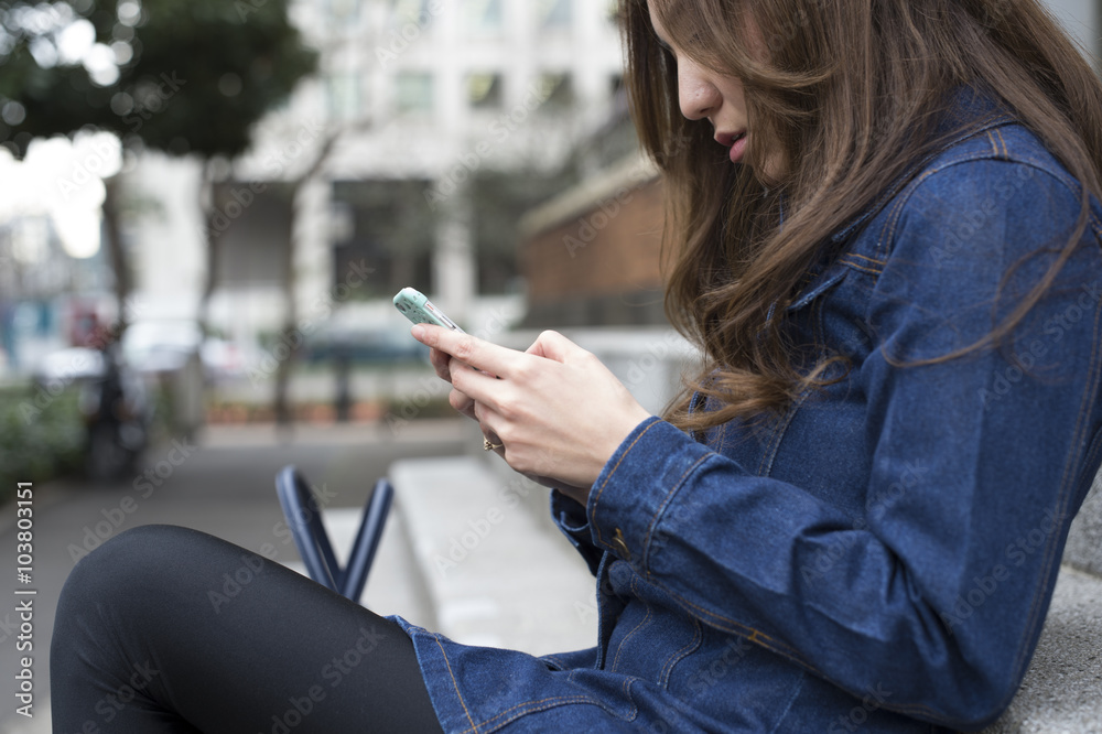 年轻女性坐在外面的楼梯上用手机互动