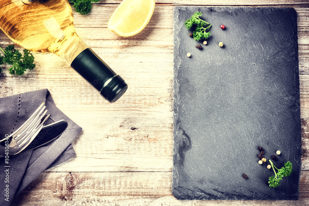 Dinner frame with bottle of white wine and cutlery on wooden tab