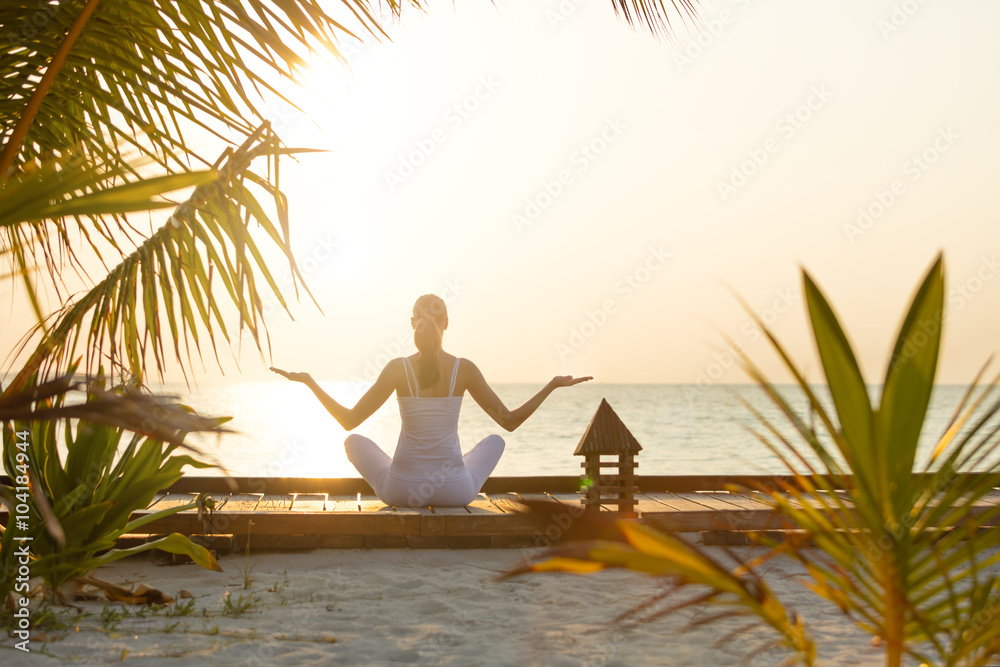 Young woman practicing yoga on the beach at sunset