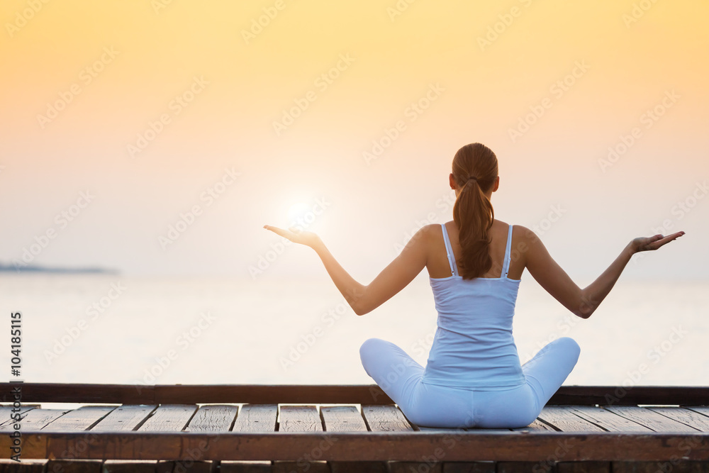 Young woman practicing yoga on the beach at sunset