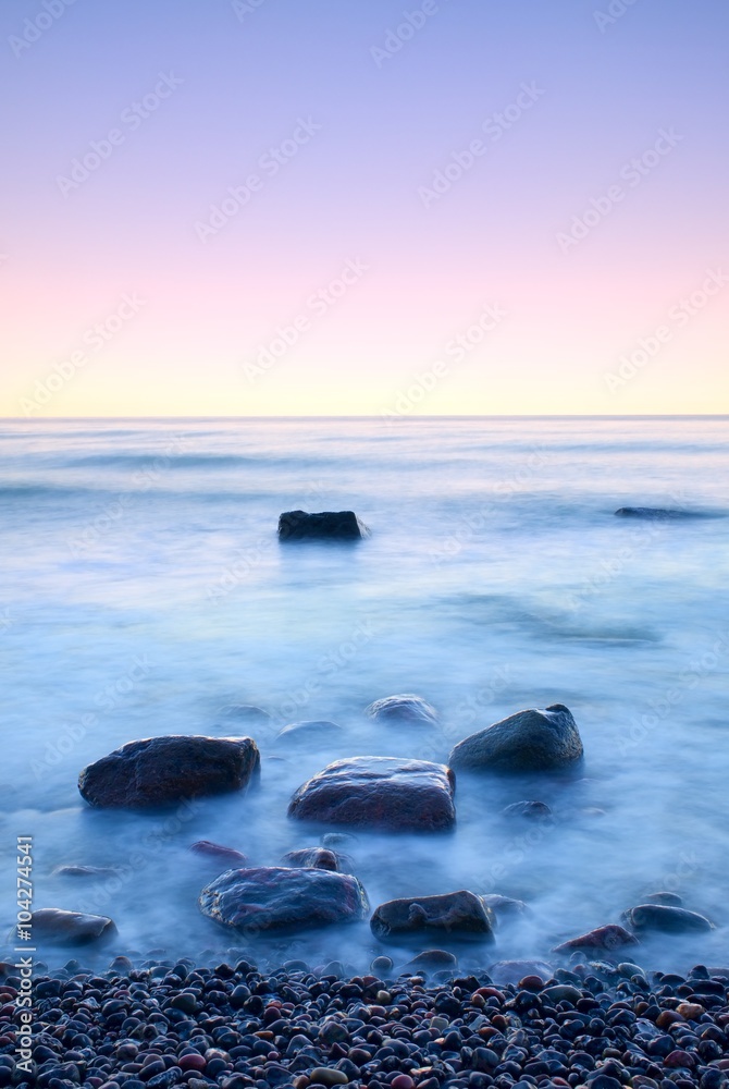 海上浪漫的早晨。大石头从光滑的波浪海中突出。长时间曝光