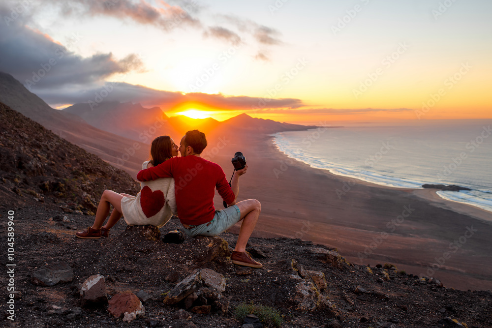 Young couple enjoying beautiful sunset sitting together on the mountain with great view on Cofete co