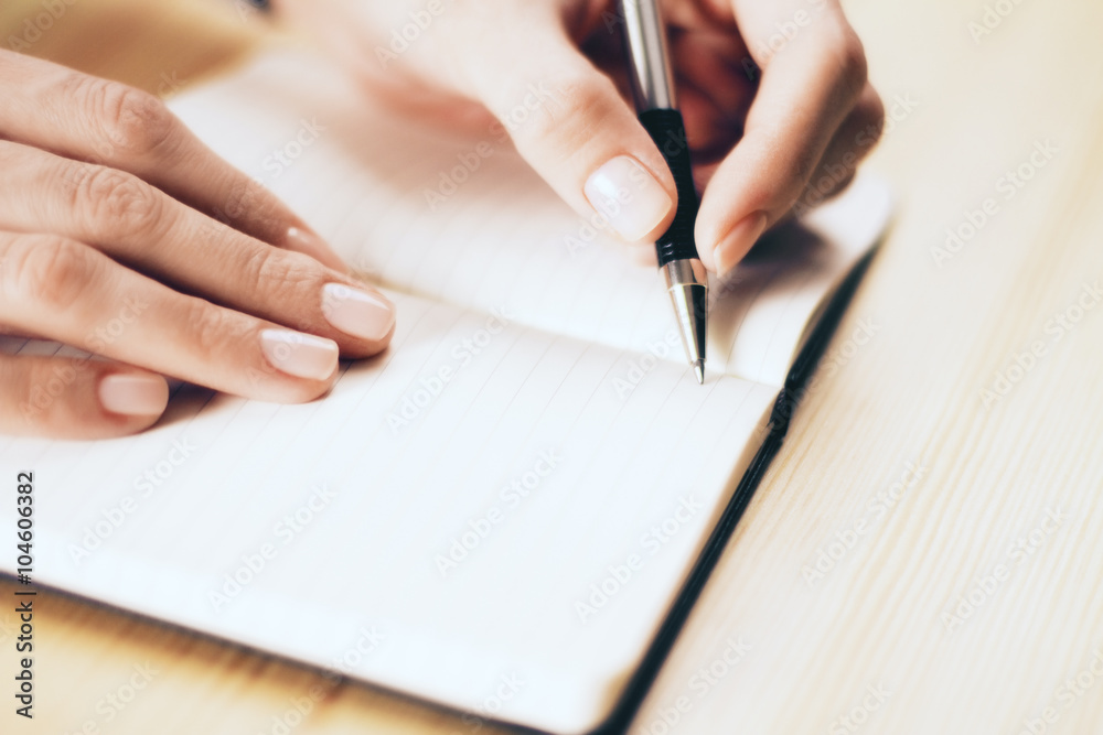 Female hands writing in notebook with pen on wooden table